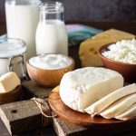 Set of different dairy products (milk, sour cream, cottage cheese, yogurt and butter) on a rustic wooden countertop.