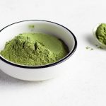 green powder in a white bowl with a spoon sitting to the side