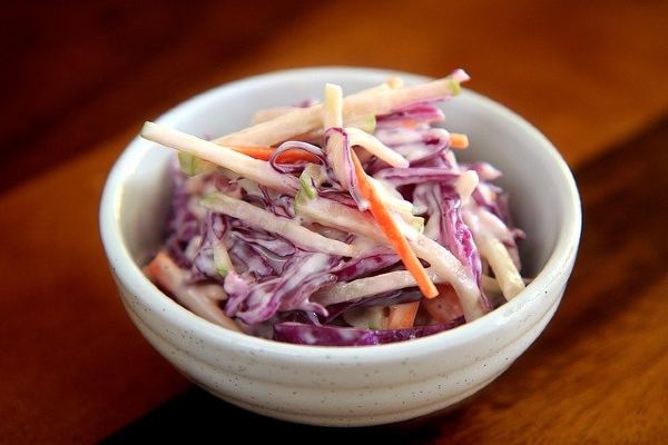 Coleslaw in a small white bowl on a wooden tabletop