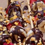 Frozen strawberries, bananas and pineapple on wooden skewers covered in chocolate and peanuts