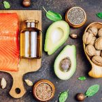 Animal and vegetable sources of healthy fats as salmon, avocado, linseed, nuts, almonds, chia seeds, spinach and olive oil on dark background. Top view.