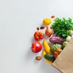 fruits and vegetables falling out of a paper bag onto a white counter