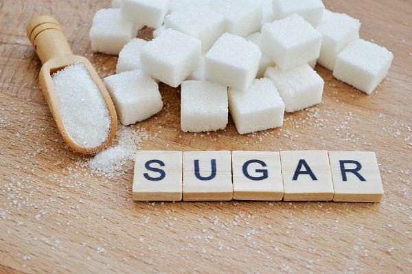 Pile of sugar cubes on a wooden surface with scrabble tiles arranged in front spelling out sugar