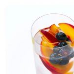 Glass of water with peaches and blueberries inside
