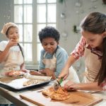 1 kid slicing pizza, one kid watching her and the other kid eating a piece of pizza