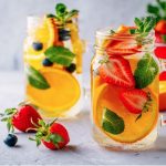 2 glasses with oranges, strawberries and mint inside the glasses surrounded by fruits