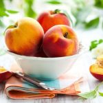 3 peaches in a white bowl with two fresh peach halves on either side of the bowl