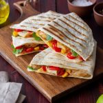 3 slices of grilled quesadilla with cheese and vegetables inside the tortilla on a wooden cutting board