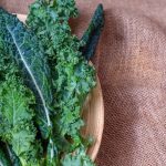 fresh kale leaves in a wooden bowl set on top of a wooden cutting surface