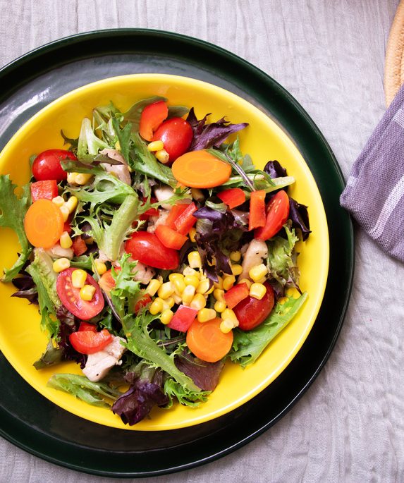 salad with tomato, lettuce, corn, and carrots in a bowl on a table