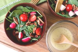 spinach salad in a bowl with pecans and tomatoes. lemon vinaigrette sits in a bowl next to it.