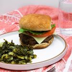 mushroom burger next to greens on a plate and a glass of water