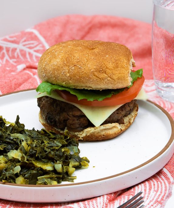 mushroom burger next to greens on a plate and a glass of water