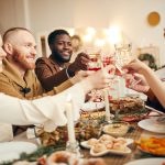 group of people sitting at dinner table with food while holding glasses up for cheers before dinner