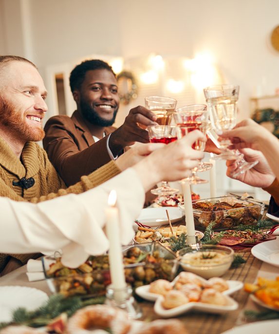 group of people sitting at dinner table with food while holding glasses up for cheers before dinner