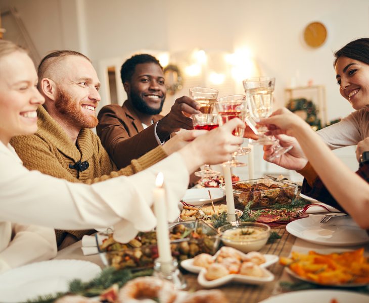 group of people sitting at dinner table with food while holding glasses up for cheers before dinner